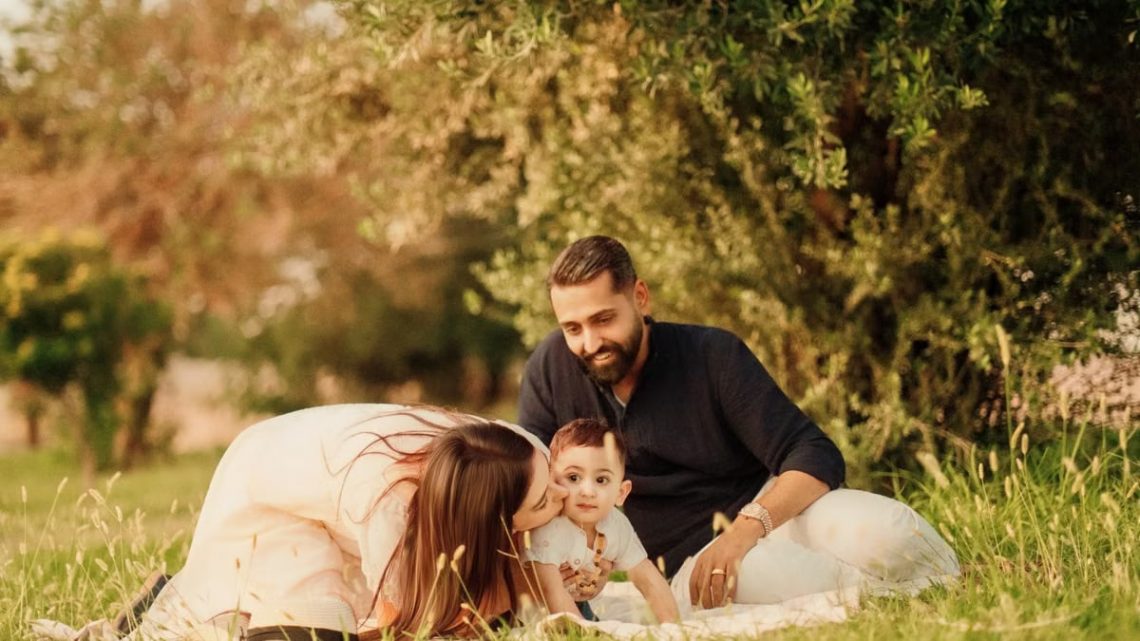 A joyful family with parents and a baby enjoying a sunny day outdoors on a picnic.